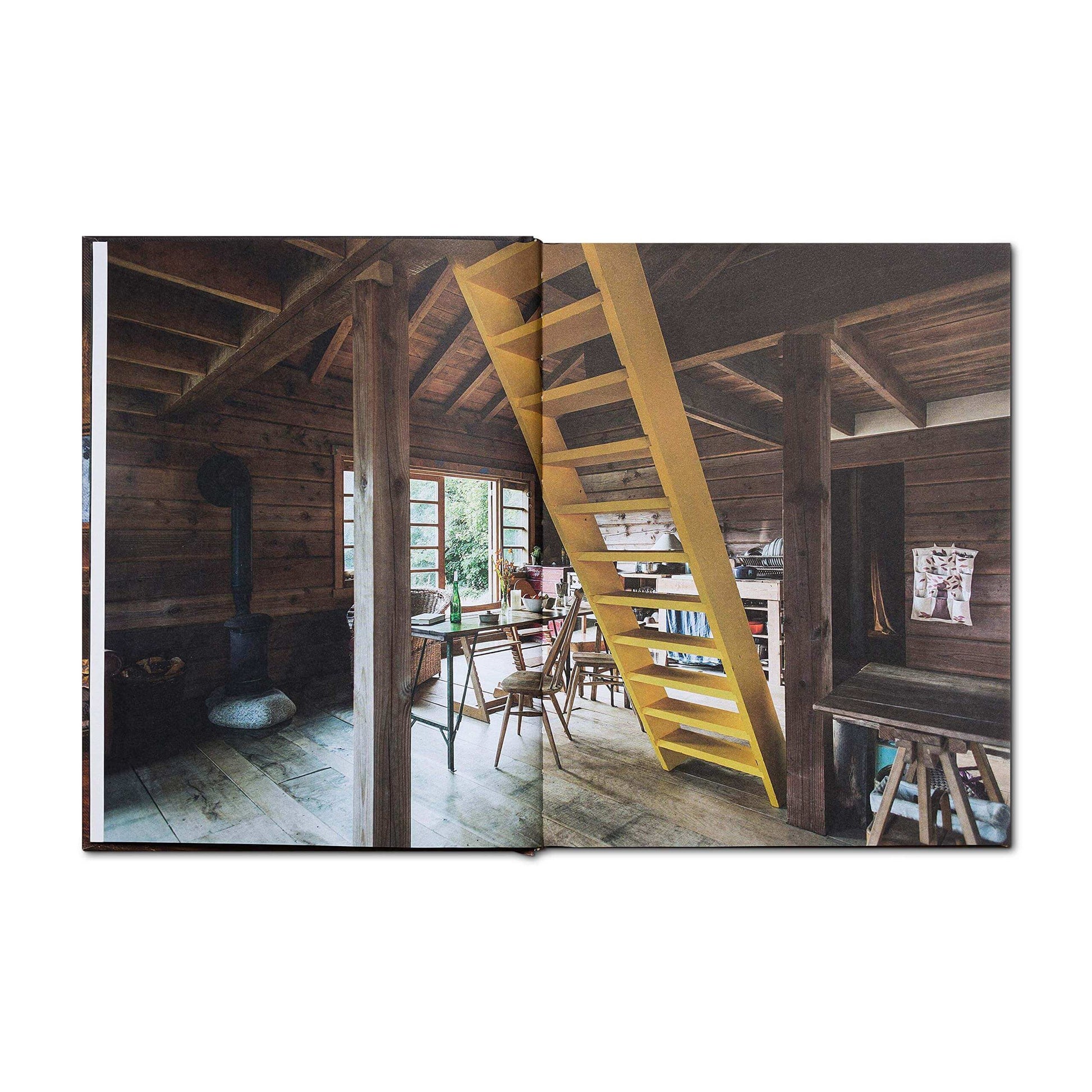 Open page of Cabin Porn Inside Book featuring rustic cabin interior with wooden beams and staircase, available at Cabin Depot.