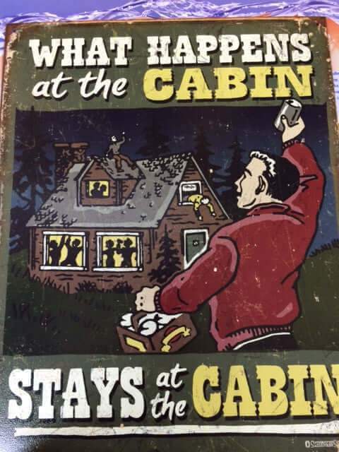 Vintage tin sign with humorous 'What Happens at the Cabin Stays at the Cabin' text, ideal for cabin decor, from Cabin Depot.
