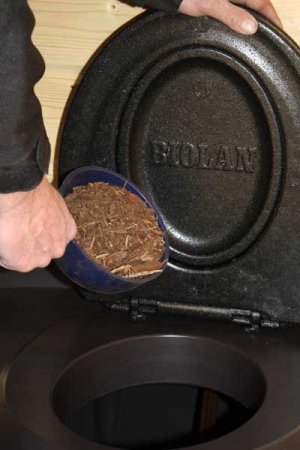 A person adding compost material to a Biolan Populett Composting Toilet from Cabin Depot, ideal for eco-friendly high-use locations.