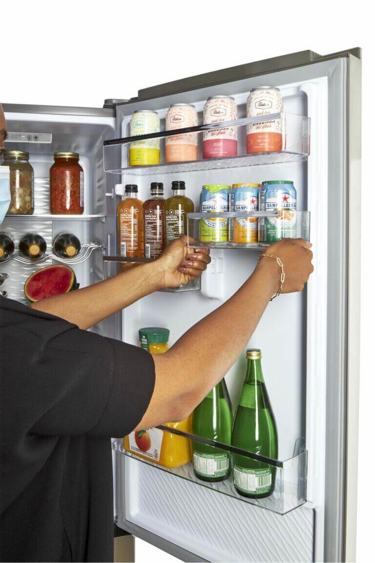 Person organizing drinks inside a Unique 12 Cu/Ft Prestige Electric Bottom Mount Refrigerator from Cabin Depot - Stainless Steel interior view.